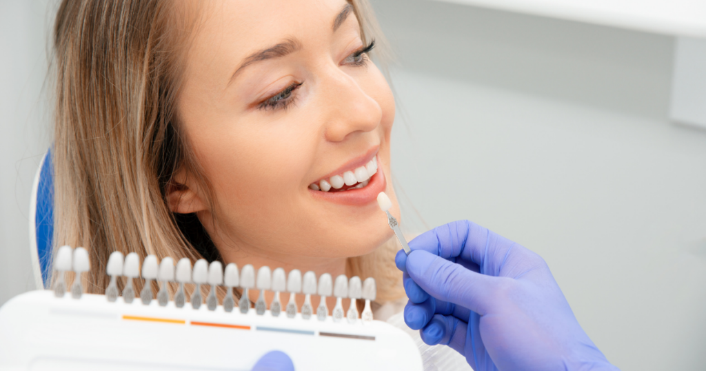 Dentist holding a shade guide against a smiling woman's teeth to select the porcelain veneer colour match.