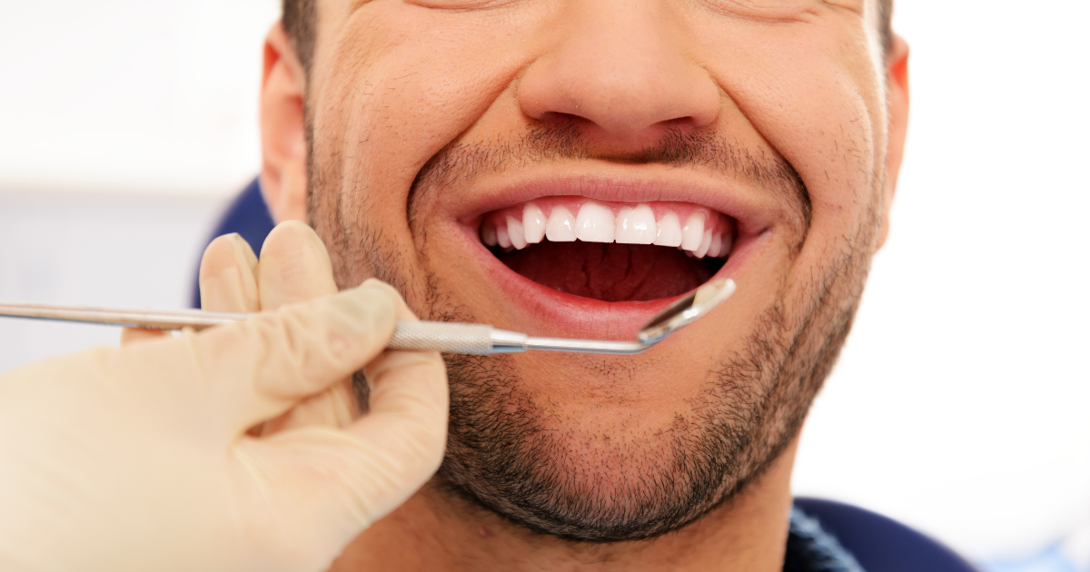 Close-up of a dentist examining a smiling patient's teeth with a dental mirror and probe