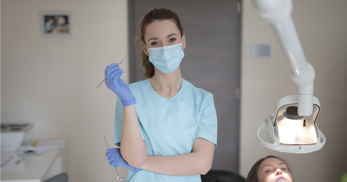 Dentist holding examination instruments beside a patient in a dental treatment room